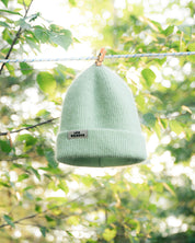 Green beanie hanging on a clothesline with a blurred natural background