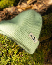 Light green beanie with a brand tag on a mossy surface