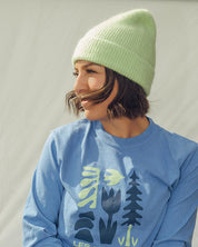 Person wearing a blue sweatshirt with 'Les Saisons' logo and a green beanie outdoors.