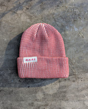 Pink beanie with a les Saisons logo on a gray concrete surface