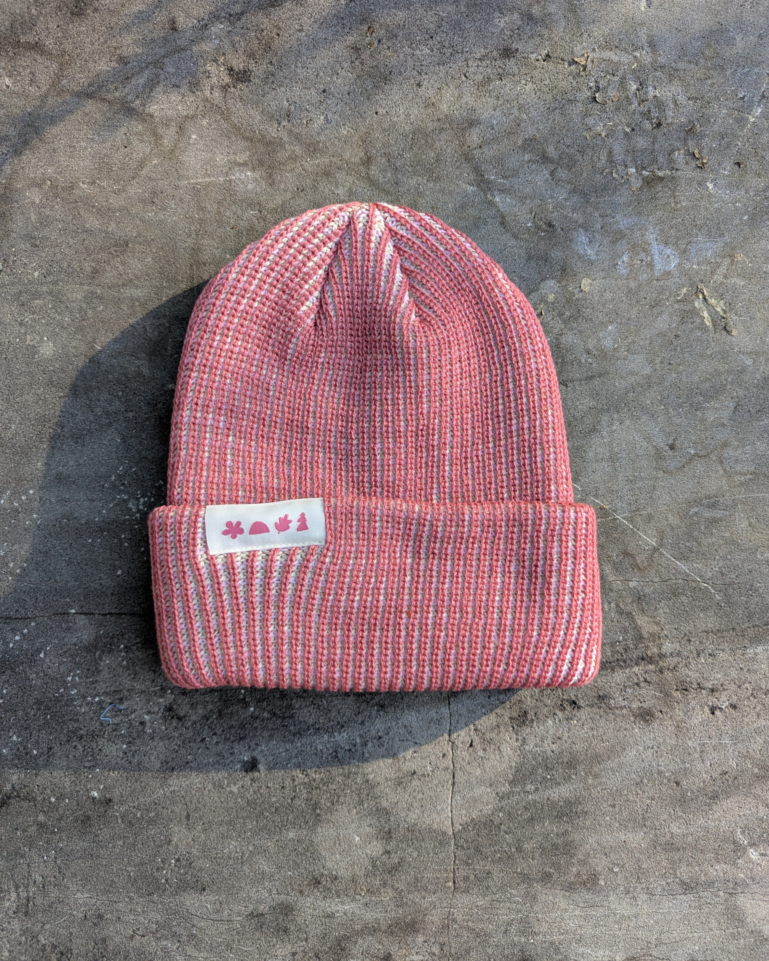 Pink beanie with a les Saisons logo on a gray concrete surface