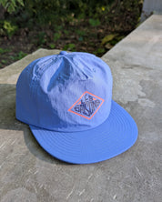 Blue cap with a logo on a concrete surface with greenery in the background