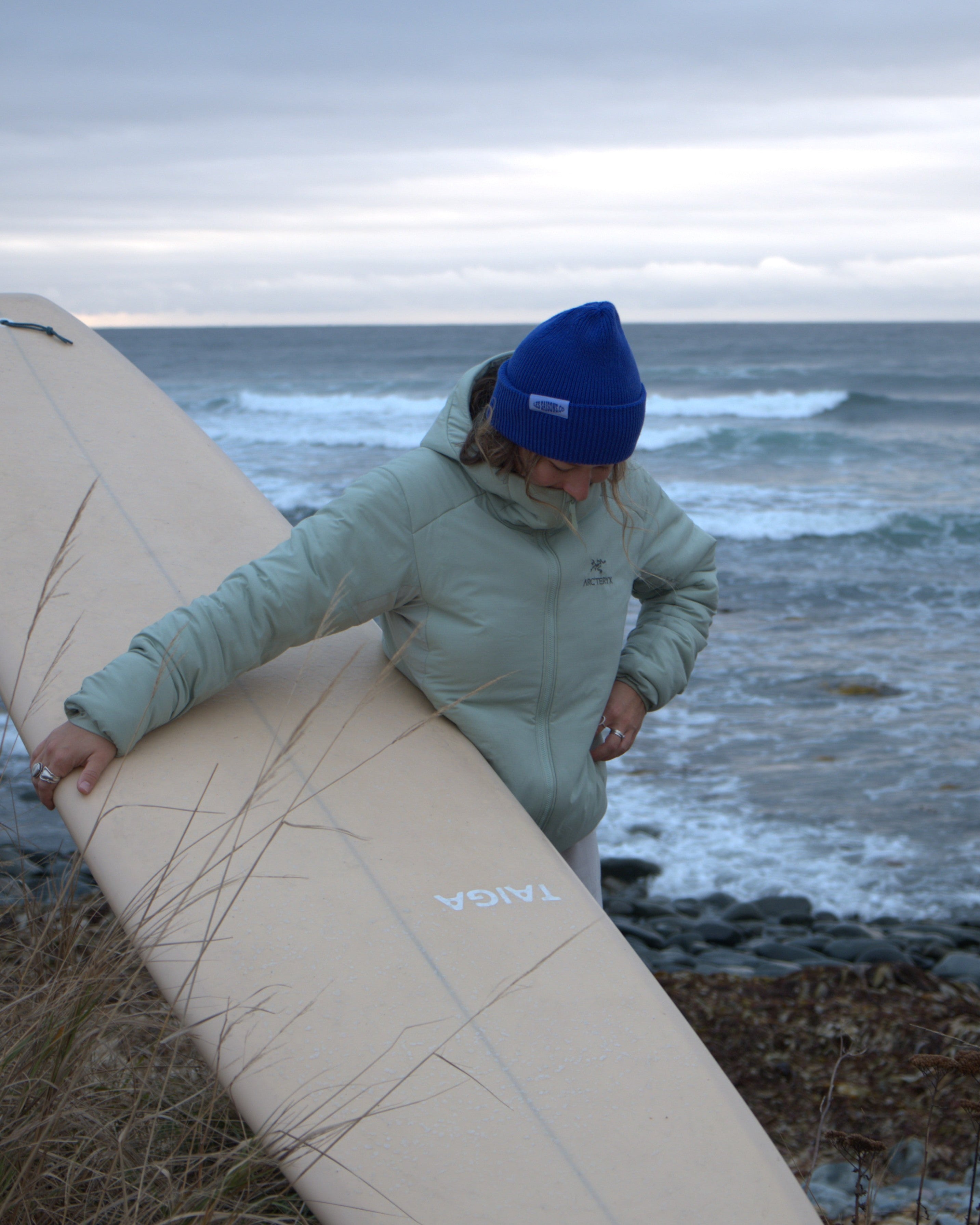Person holding a surfboard by the ocean on a cloudy day