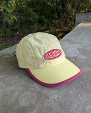 Light green cap with pink brim and logo on a stone surface with blurred greenery in the background