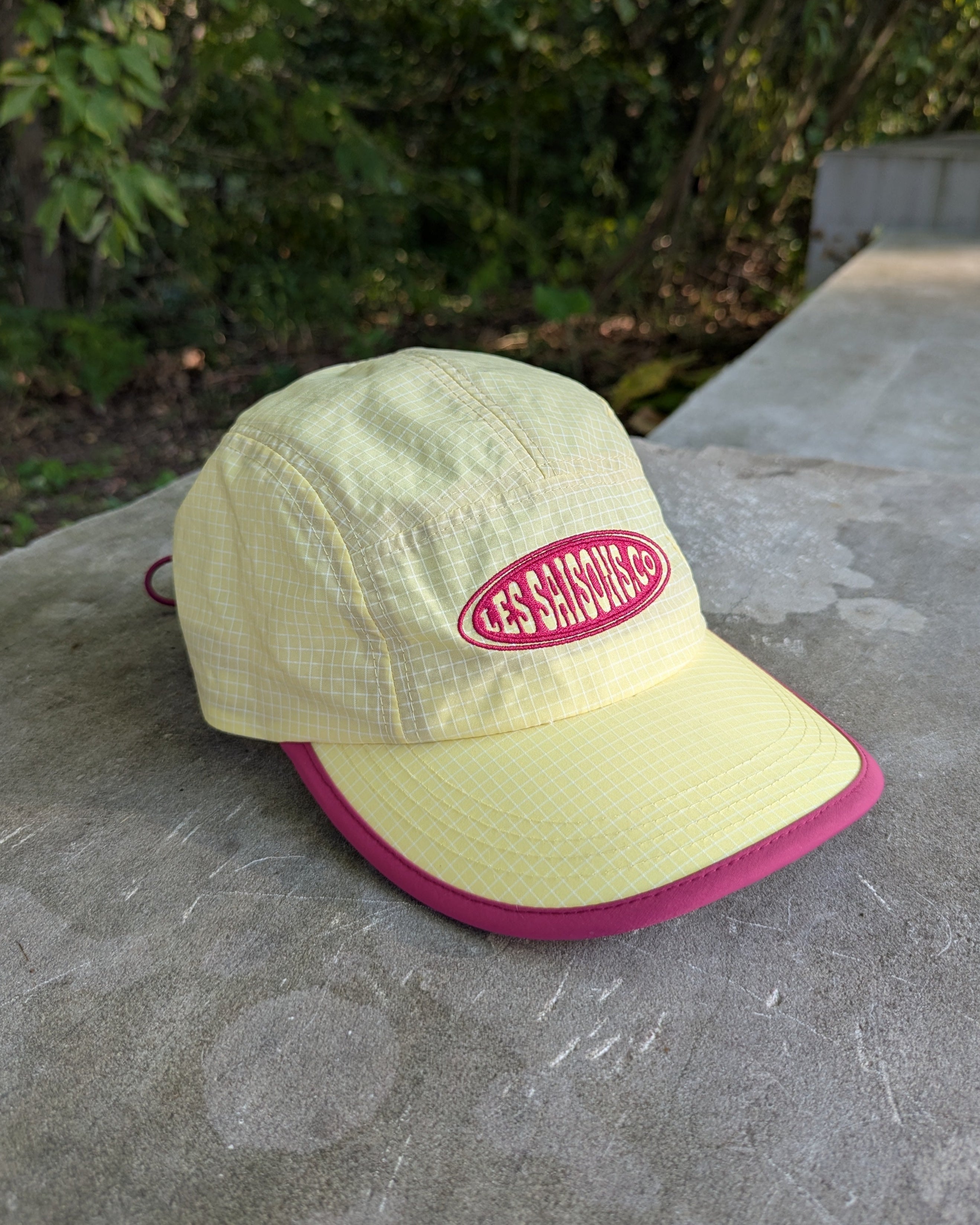 Light green cap with pink brim and logo on a stone surface with blurred greenery in the background