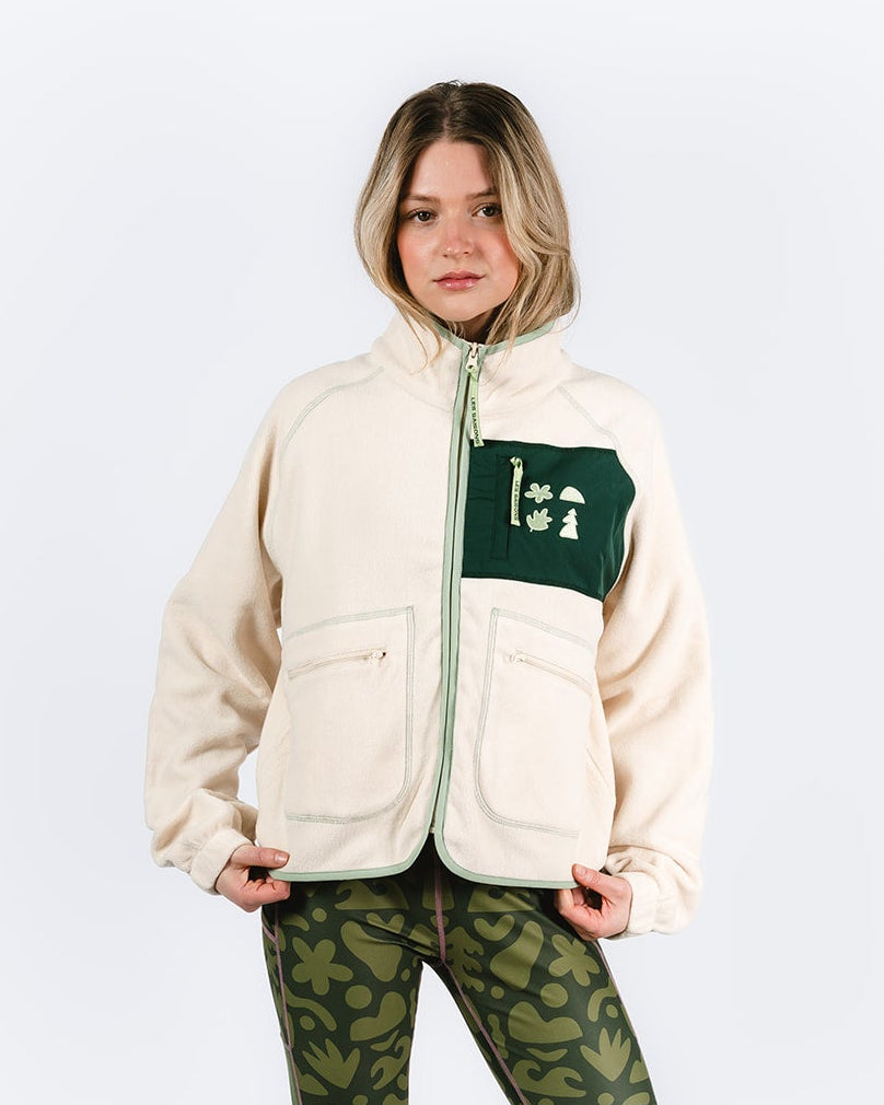 Person wearing a cream fleece jacket with a green  les Saisons logo, green camouflage pants, and beige boots on a white background