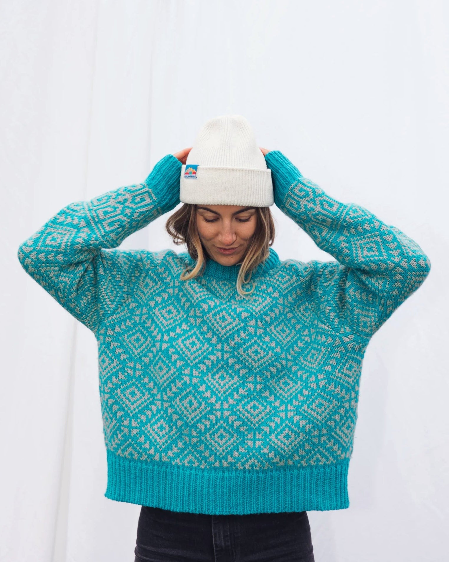 Person wearing a teal patterned Merino sweater and white beanie against a white background