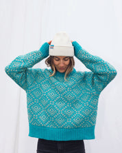 Person wearing a teal patterned Merino sweater and white beanie against a white background