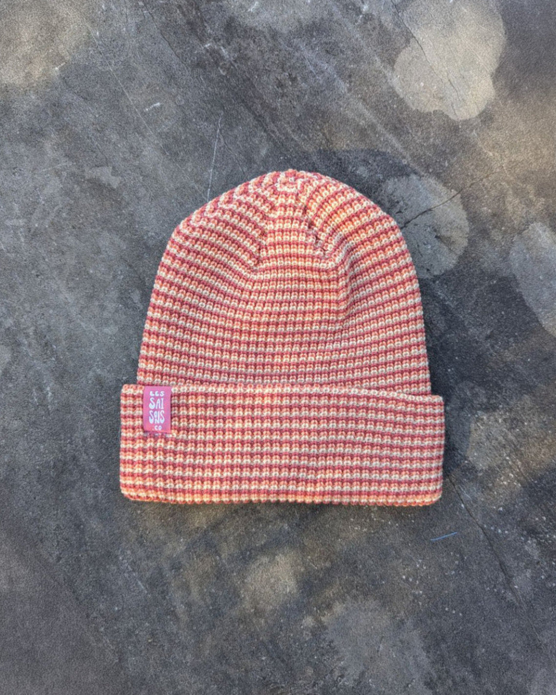blush beanie with a pink les Saisons tag on a gray concrete surface, made in Canada.