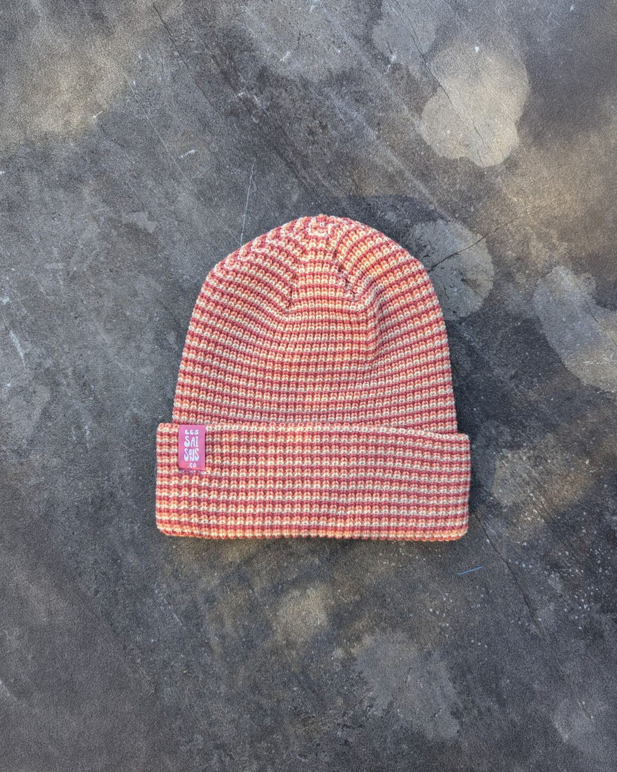 blush beanie with a pink les Saisons tag on a gray concrete surface, made in Canada.