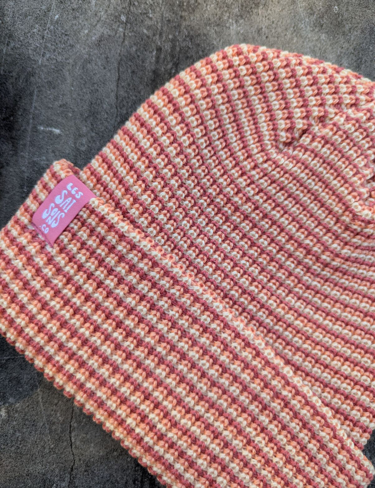 zoom on the blush beanie with a pink les Saisons tag on a gray concrete surface, made in Canada.