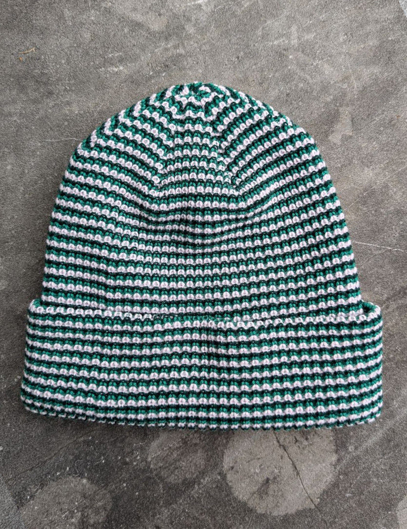 Green beanie with a les Saisons tag on a gray concrete surface, made in Canada.