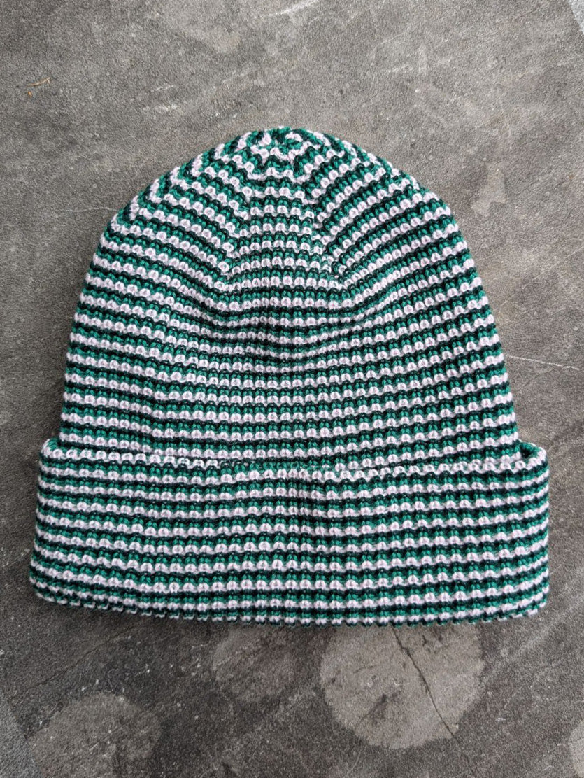 Green beanie with a les Saisons tag on a gray concrete surface, made in Canada.