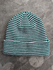 Green beanie with a les Saisons tag on a gray concrete surface, made in Canada.