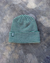 Green beanie with a green les Saisons tag on a gray concrete surface, made in Canada.