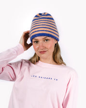 Person wearing a striped beanie and pink sweatshirt with 'LES SAISONS CO' text on a white background