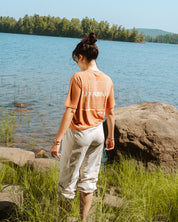 Woman standing by a lake with trees in the background_ With a Brown crop t-shirt les Saisons