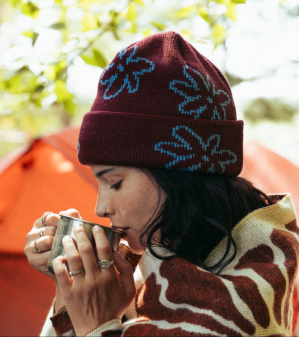 Woman wrapped up in blanket wearing dark red beanie with light blue flower pattern 