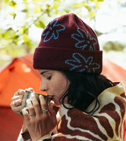 Woman wrapped up in blanket wearing dark red beanie with light blue flower pattern 