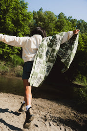 Girl runningi with a green and cream blanket on her shoulder with a tree and sun pattern