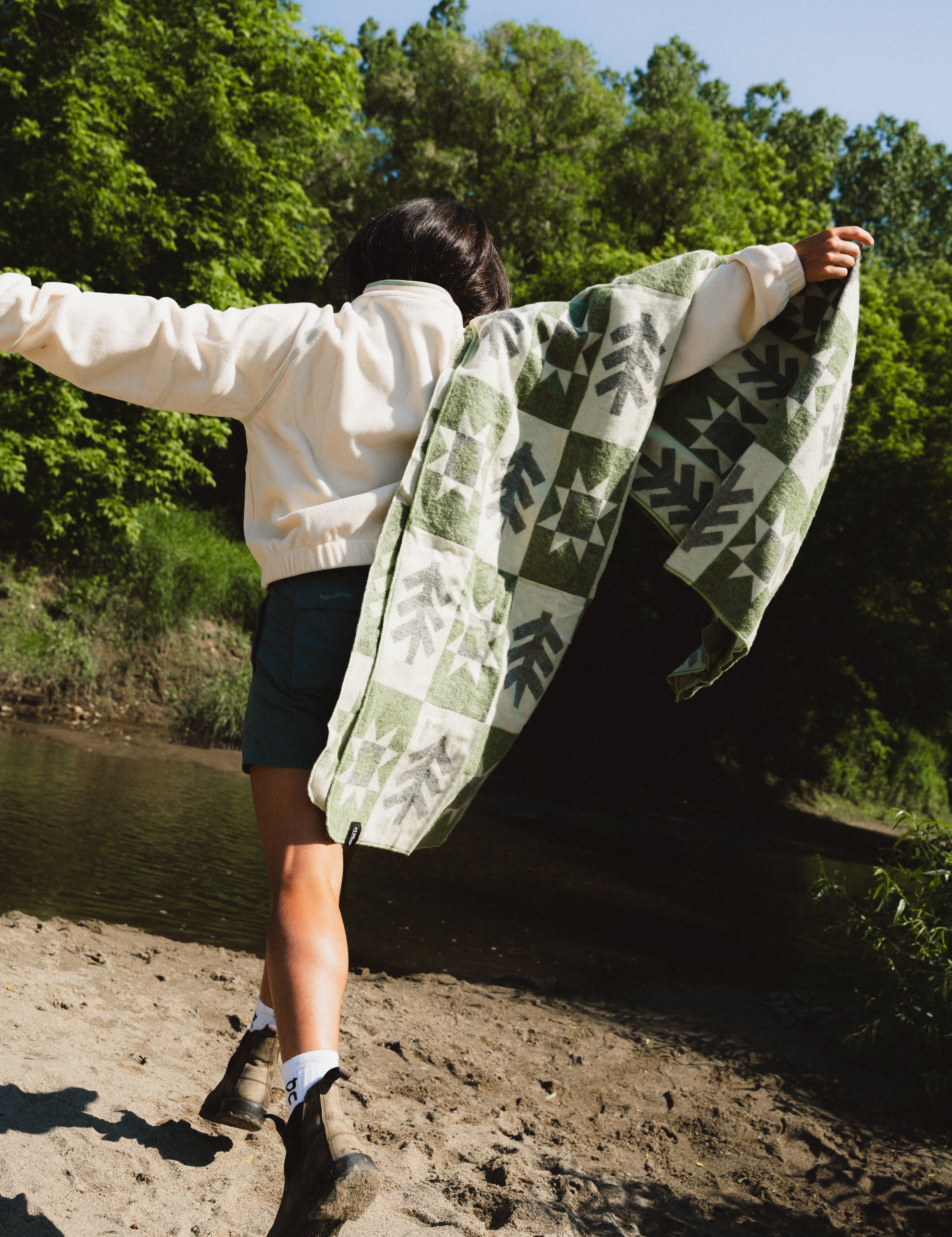 Girl runningi with a green and cream blanket on her shoulder with a tree and sun pattern