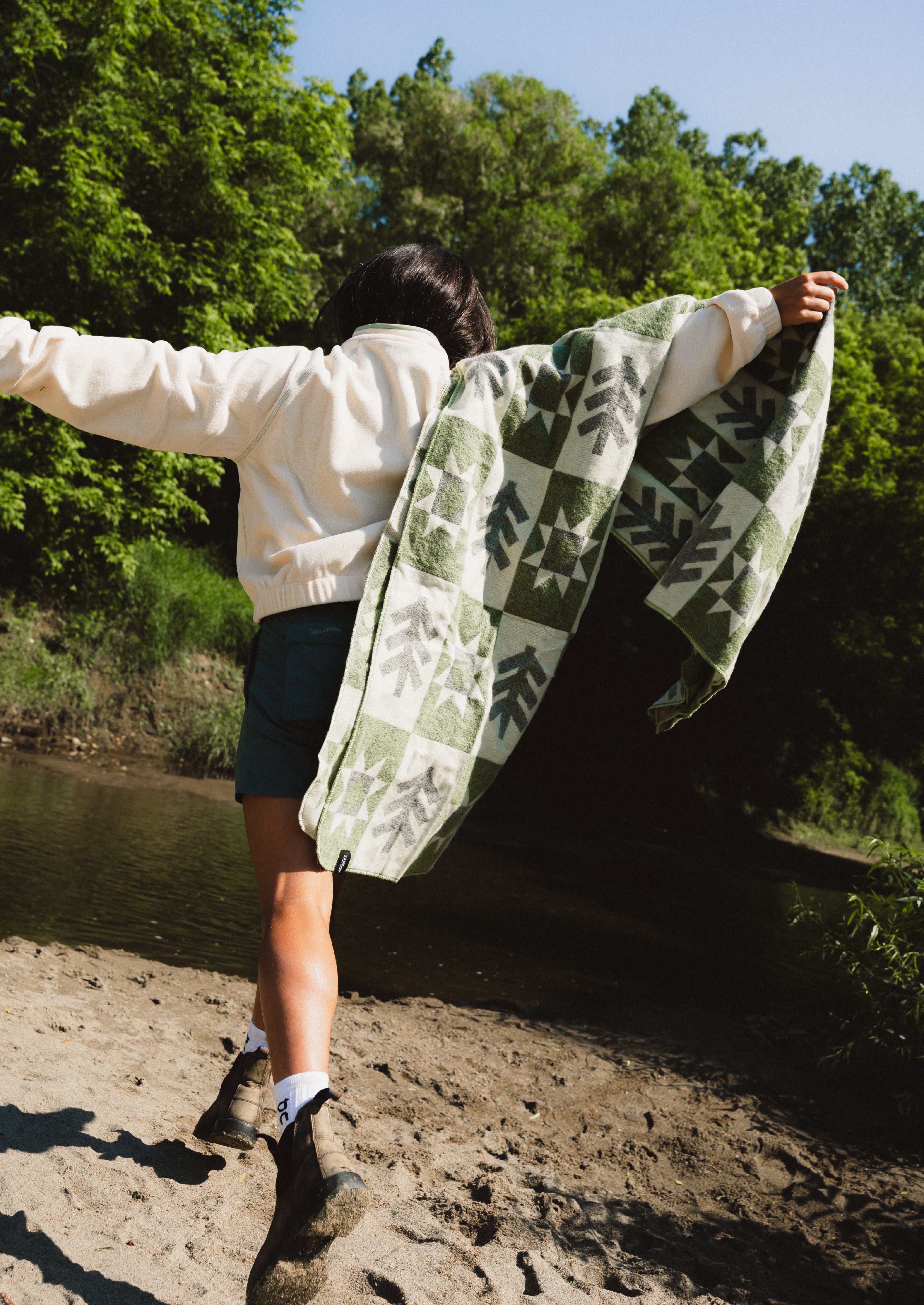 Girl runningi with a green and cream blanket on her shoulder with a tree and sun pattern