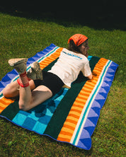 Girl laying on a blanket with blue and orange geometric pattern with a grass background