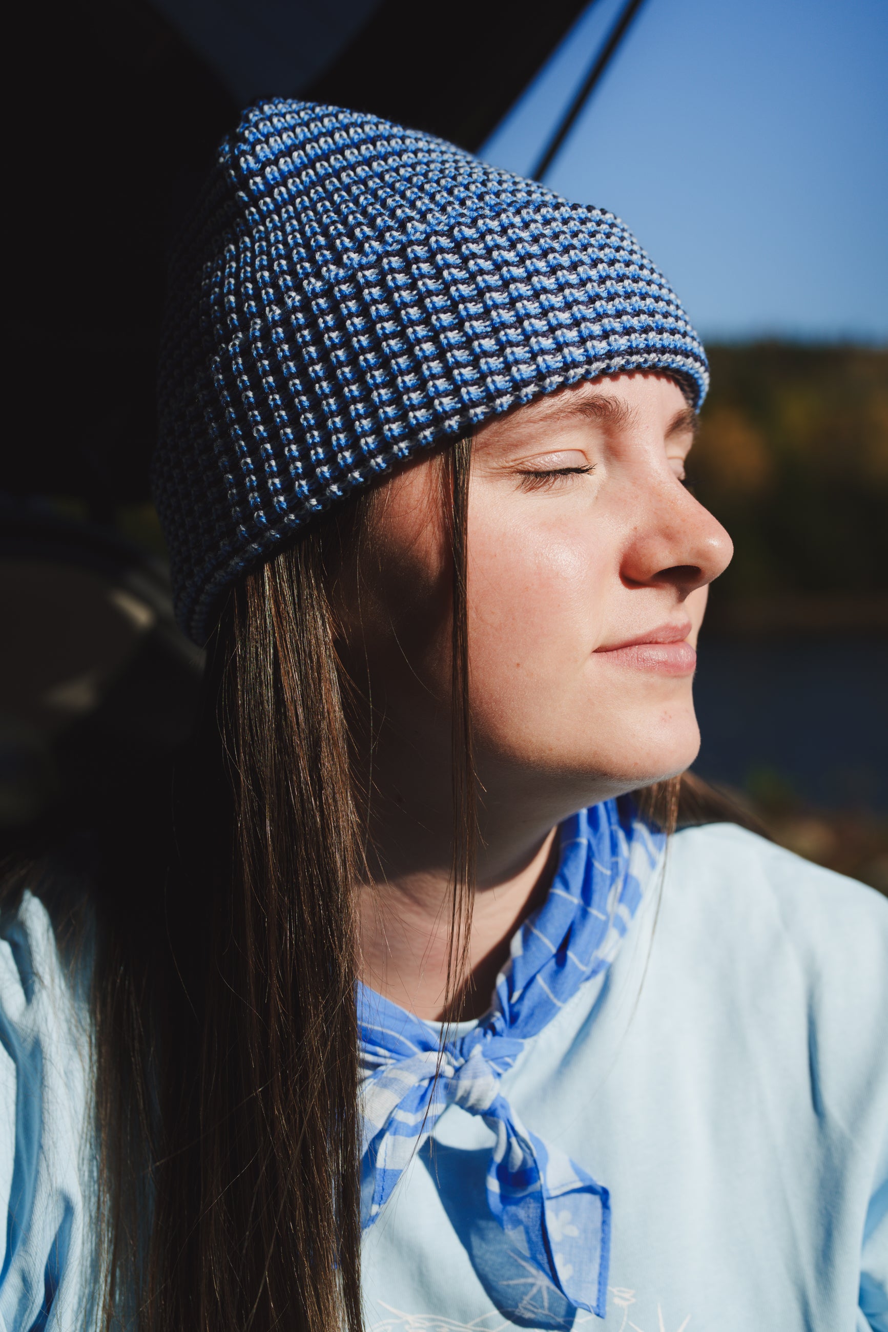 Person wearing the LesSaisons Blue Lines knit beanie with a folded cuff, shown in side profile with eyes closed in sunlight