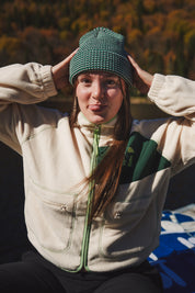 Person wearing the LesSaisons Green Lines beanie in green and white knit, holding both hands to the hat outdoors.