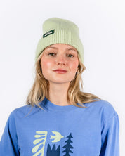 Person wearing a blue sweatshirt with 'Les Saisons' design and a light green Mohair beanie on a white background