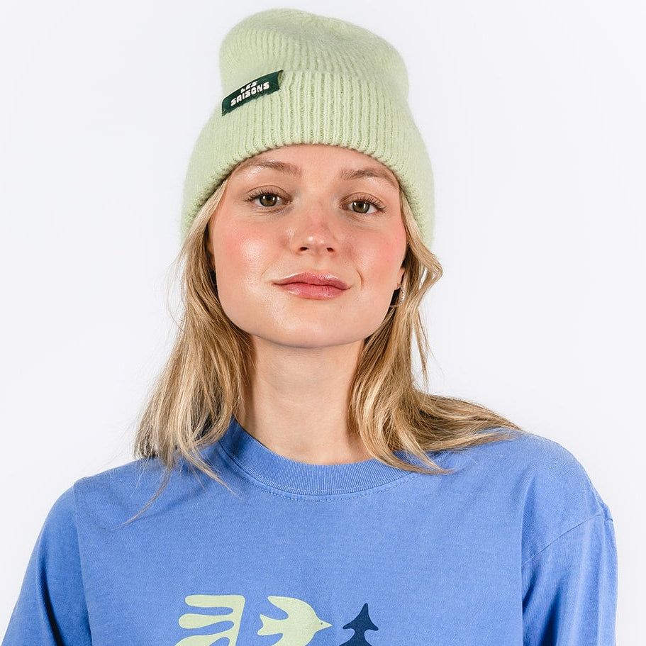 Person wearing a blue sweatshirt with 'Les Saisons' design and a light green Mohair beanie on a white background