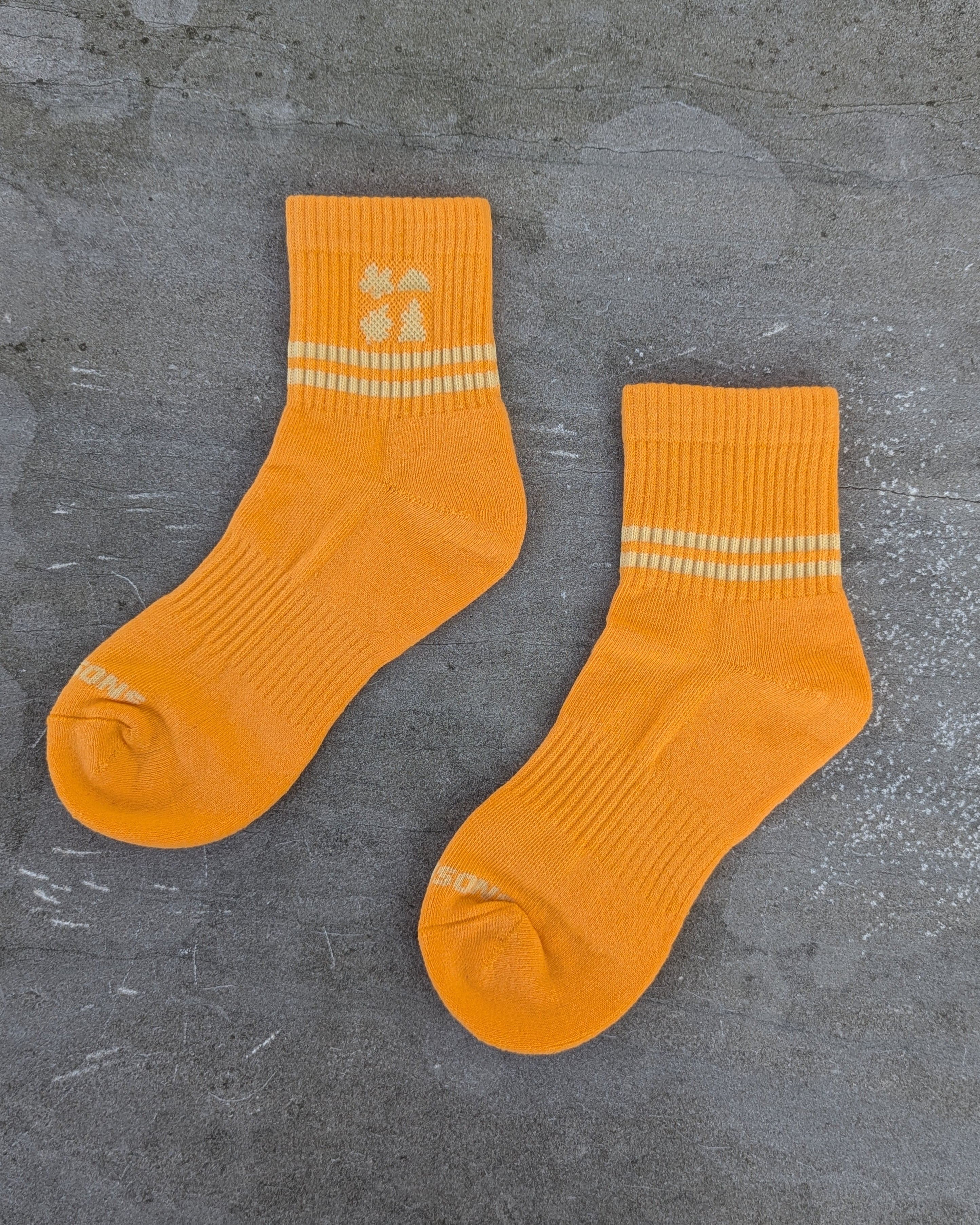 Pair of orange socks pilates and sport les Saisons with Cream stripes on a gray concrete surface