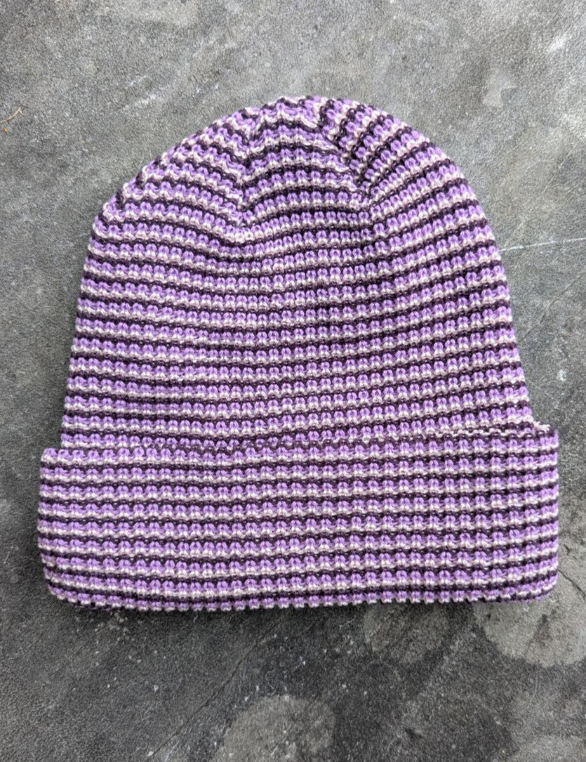 Purple beanie with a les Saisons tag on a gray concrete surface, made in Canada.