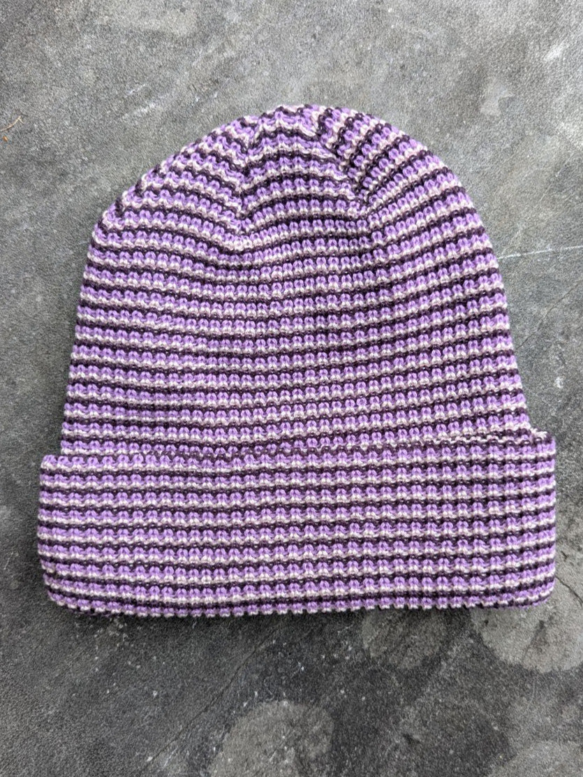 Purple beanie with a les Saisons tag on a gray concrete surface, made in Canada.