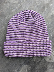 Purple beanie with a les Saisons tag on a gray concrete surface, made in Canada.