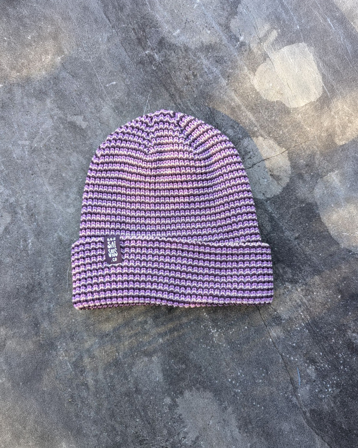 Purple beanie with a purple les Saisons tag on a gray concrete surface, made in Canada.