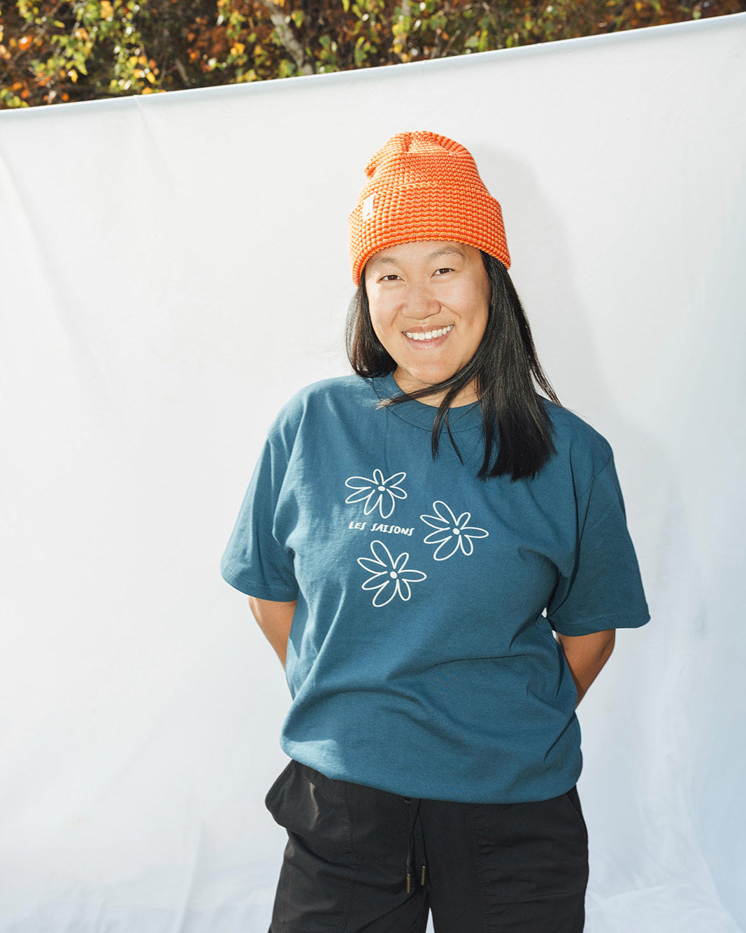 Person wearing a blue t-shirt with white floral designs and an orange beanie standing against a white background.