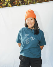 Person wearing a blue t-shirt with white floral designs and an orange beanie standing against a white background.