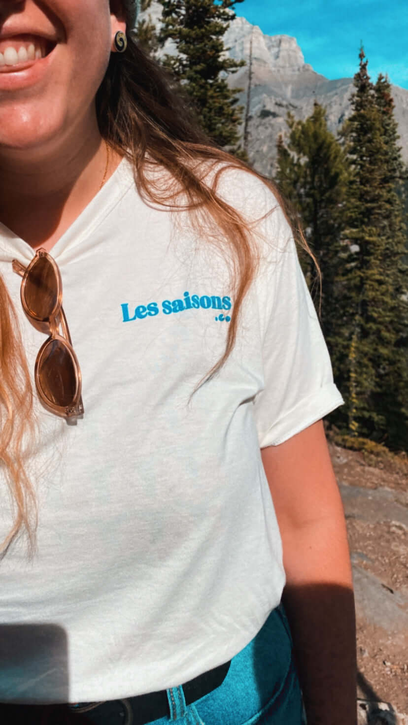 Person smiling in white soft bamboo t-shirt with Les Saisons. co logo in blue.
